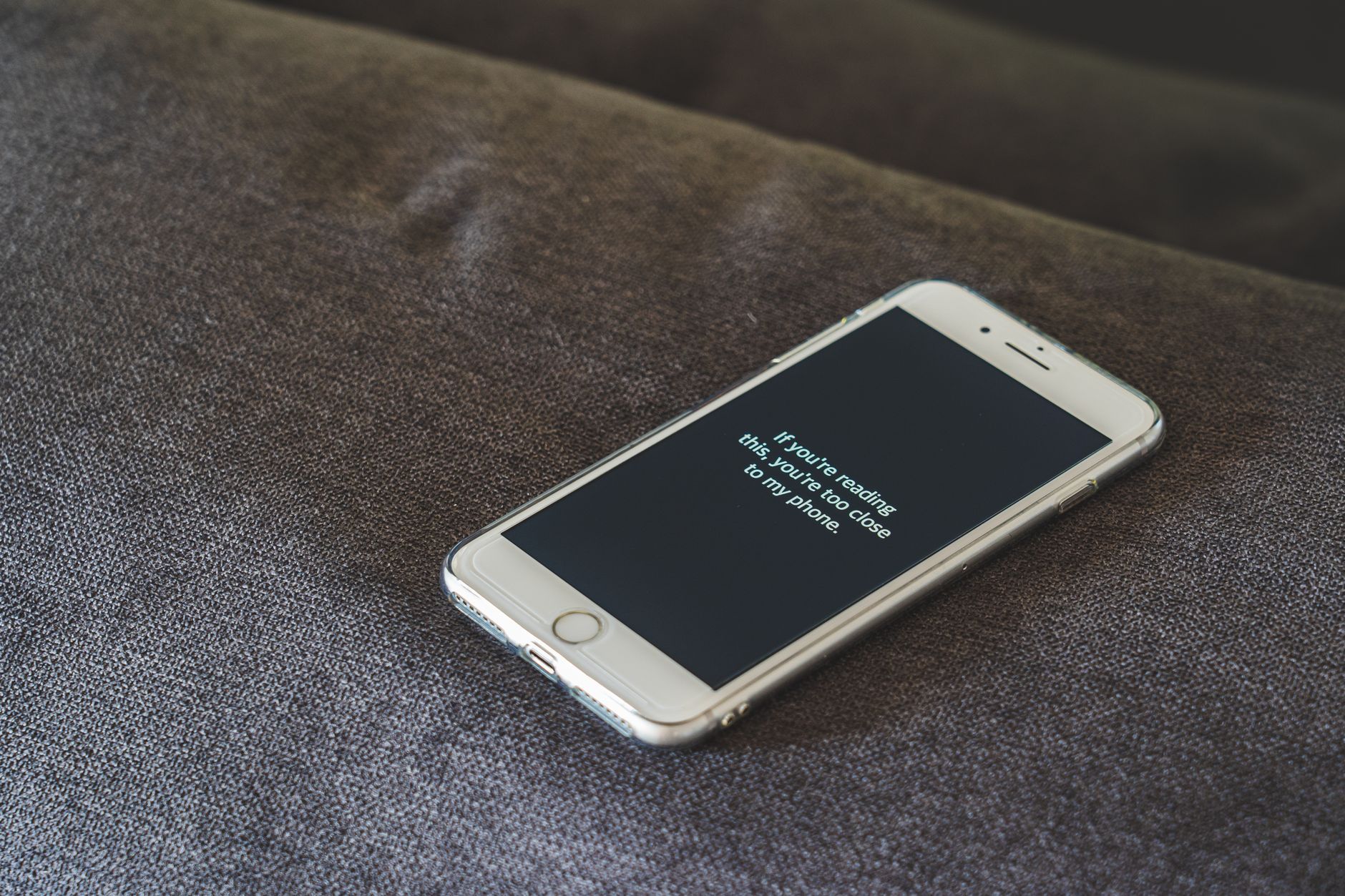 A smartphone with a humorous lock screen message placed on a grey couch, emphasizing privacy.
